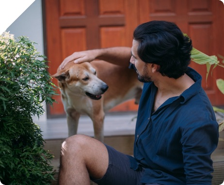 Man sits on the front steps of his home and pets a yellow dog on the head. 